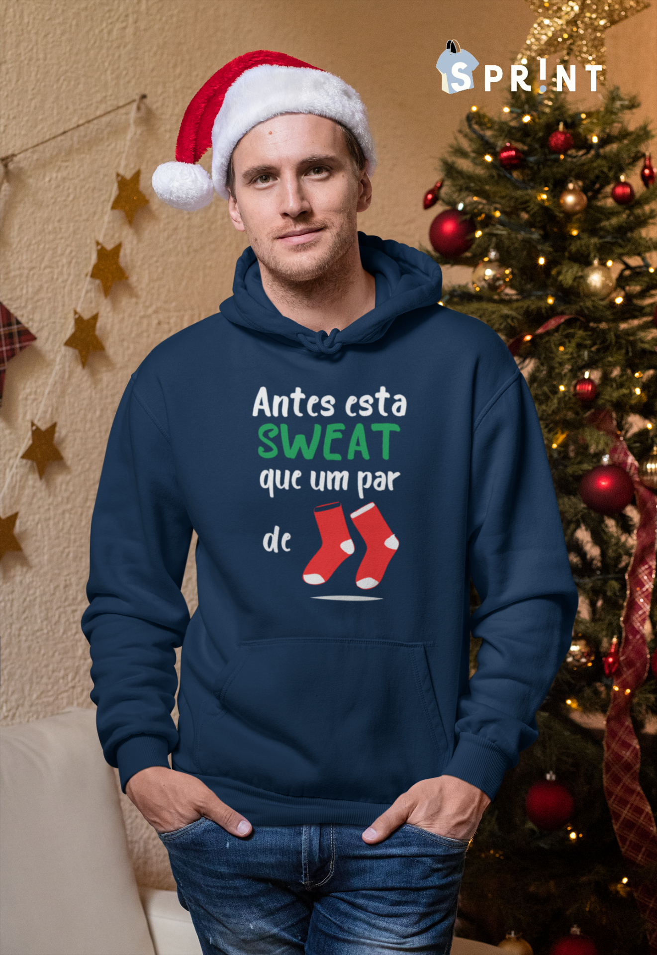 Homem com camisola azul de capuz e gorro de Natal junto a árvore decorada