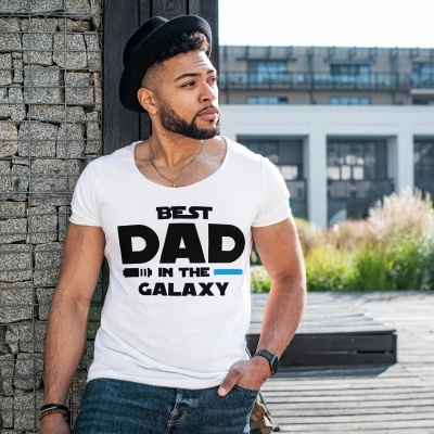 Homem usando camisola branca com texto 'BEST DAD IN THE GALAXY' encostado a coluna de pedra