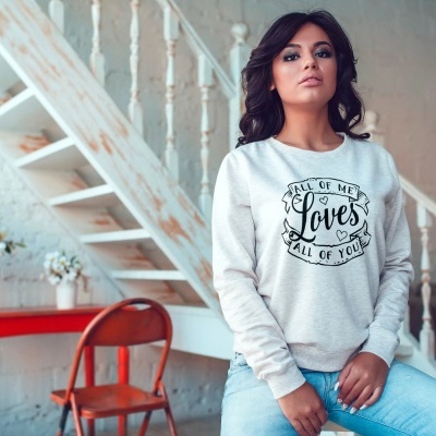 Mulher com sweatshirt cinza e calças jeans sentada em ambiente com escada branca e móveis coloridos