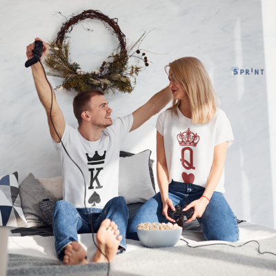 Casal a jogar videojogos com t-shirts de rei e rainha de baralho sentados no sofá