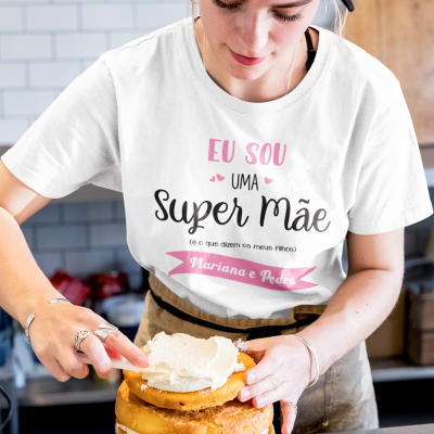 Mulher a decorar bolo com t-shirt personalizada 'Super Mãe' numa cozinha