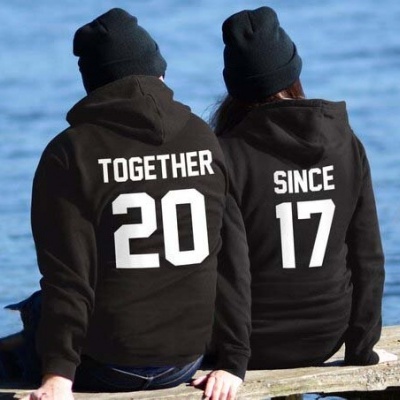 Duas pessoas com sweatshirts pretas com textos em branco sentadas junto a água