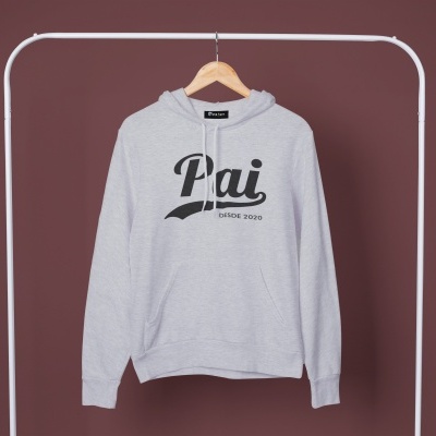 Camisola cinzenta clara de capuz com texto preto 'Pai DESDE 2020' pendurada em cabide num suporte branco.