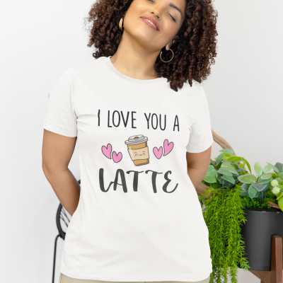 Mulher a usar t-shirt branca com estampa 'I LOVE YOU A LATTE' e calças bege, em ambiente interior com plantas.