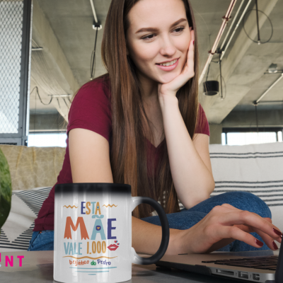 Caneca branca e preta com texto colorido ao lado de rapariga usando portátil