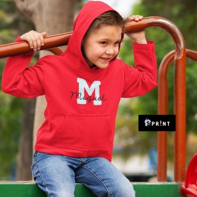 Criança com camisola vermelha com capuz e estampa 'M Miguel', sentada em parque infantil