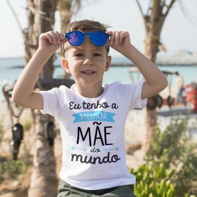 Camiseta branca com texto em português usada por menino na praia
