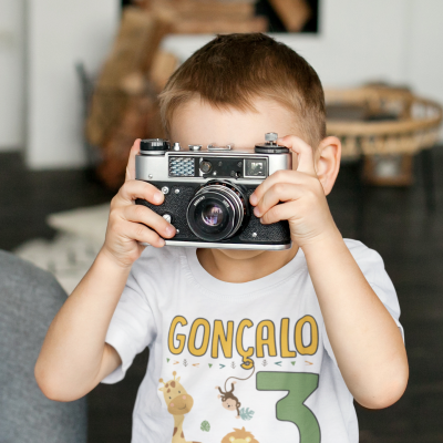 Criança com camisola branca estampada segurando uma câmara fotográfica vintage cinzenta e preta