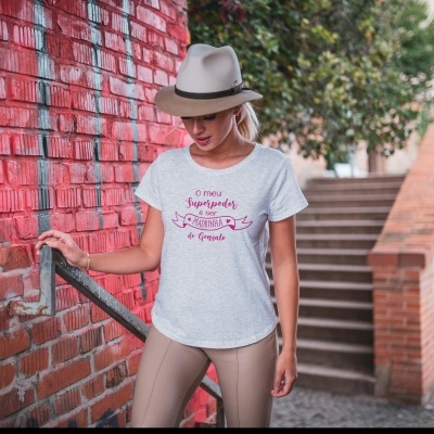 Mulher usando t-shirt cinza com texto em rosa e vermelho em ambiente exterior com parede vermelha de tijolos