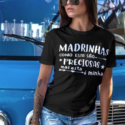 Mulher com t-shirt preta com texto branco e calções de ganga, junto a carrinha azul clássica