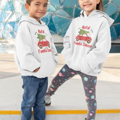 Duas crianças com sweatshirts brancas com capuz estampadas com carro vermelho e árvore de Natal verde em ambiente exterior