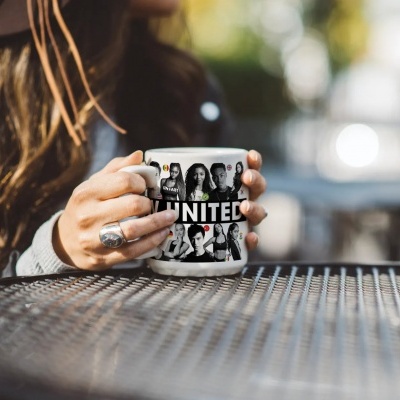 Caneca branca com fotos a preto e branco e texto UNITED, numa mão sobre mesa metálica