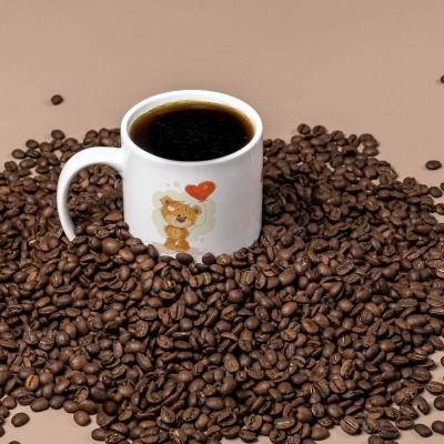 Caneca branca com ilustração de urso e balão vermelho, cheia de café preto, rodeada por grãos de café