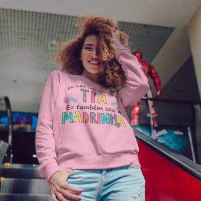 Mulher com sweatshirt rosa com texto colorido sobre ser tia e madrinha.
