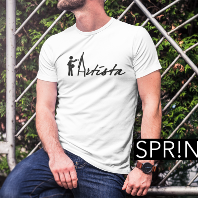 Homem com t-shirt branca 'Artista' sentado junto a cerca metálica com plantas