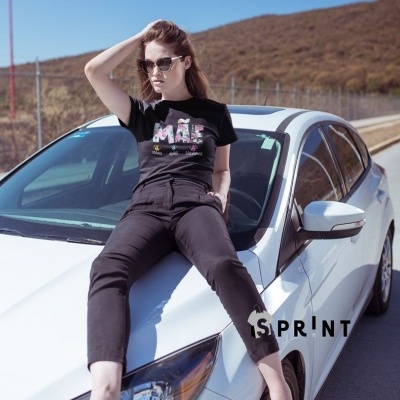 Mulher sentada no capot de um carro branco com t-shirt preta e calças pretas