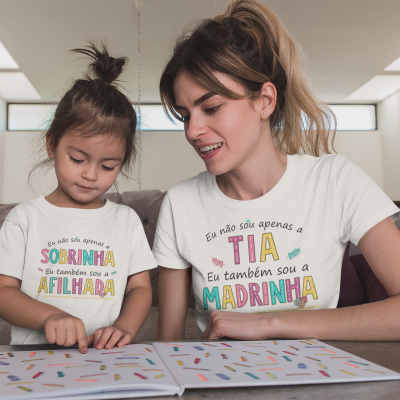 Camisetas brancas com texto colorido com frases familiares, criança e mulher sentadas a ler livro numa sala.