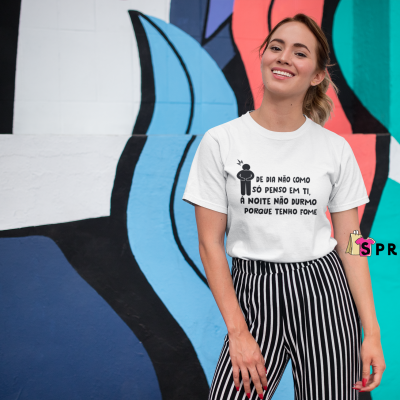 Mulher com t-shirt branca com texto preto e calças de riscas junto a muro com grafiti colorido.