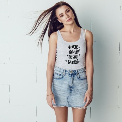 Mulher com t-shirt cinza clara e saia de ganga azul clara junto a parede branca