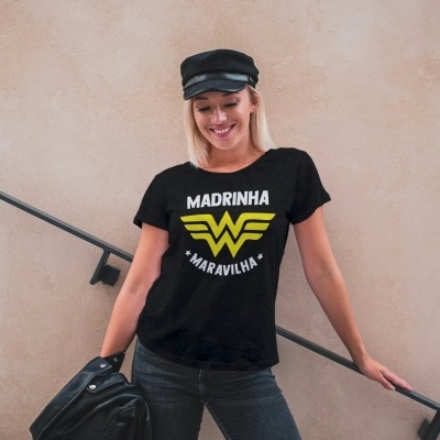 Mulher com camisola preta estampada 'MADRINHA MARAVILHA' e boina preta encostada na escada.