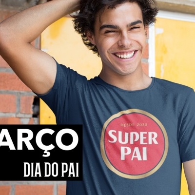 Homem sorridente com camisola azul 'SUPER PAI' em fundo amarelo e parede de tijolos vermelhos