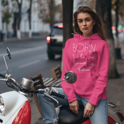 Mulher com sweatshirt rosa com texto branco sentada numa mota numa rua da cidade