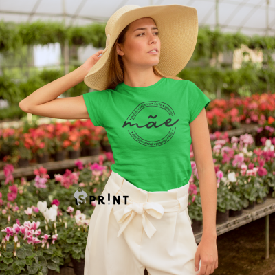 Mulher com t-shirt verde estampada, calças brancas largas e chapéu de palha, em estufa com flores