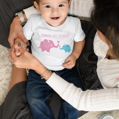 Bebé com camisola estampada de elefantes e texto sentado no colo da mãe