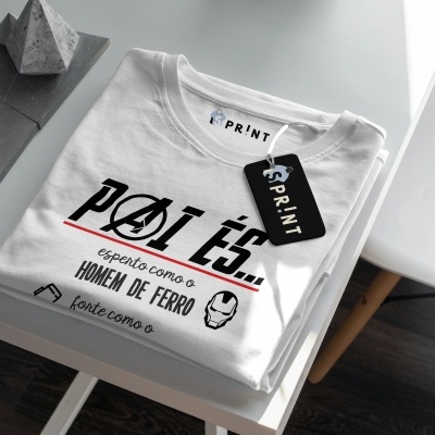 Camiseta branca com estampa 'PÓI ÉS... Homem de Ferro' dobrada sobre mesa branca
