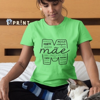 Mulher com t-shirt verde clara com texto em preto sentado numa cama ao lado de um gato branco e cinzento