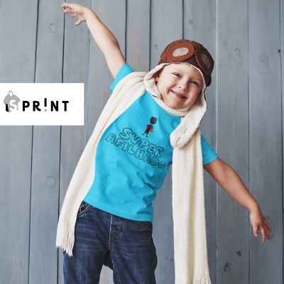 Menino com camisola azul 'SUPER AFILHINHO', calças de ganga, cachecol bege e chapéu de aviador castanho, fundo madeira cinzenta.