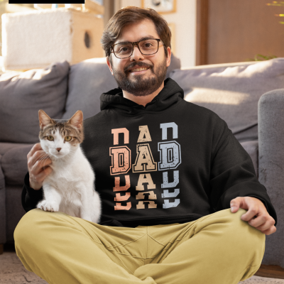 Homem sentado no chão com hoodie preto com letras 'DAD' coloridas e gato no colo