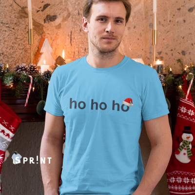 Homem com t-shirt azul clara com texto 'ho ho ho' e chapéu de Natal, ambiente natalício com lareira e decoração