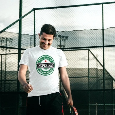 Homem com t-shirt branca com mensagem dia do pai, calça preta, segurando raquete de ténis numa quadra de ténis