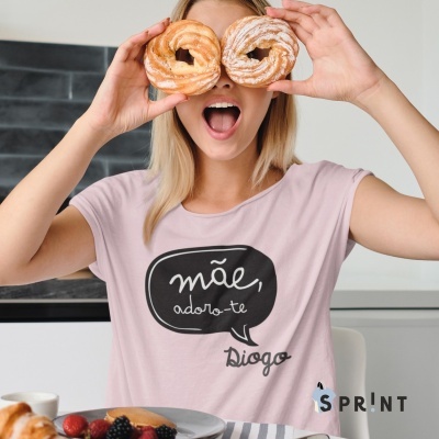 Pessoa segurando dois doces, t-shirt rosa com texto e mesa com frutas.