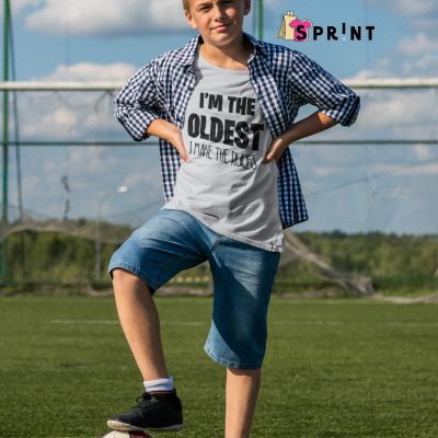 Rapaz no campo de futebol com pé sobre bola, vestindo camisa xadrez, t-shirt cinza com texto e calções de ganga