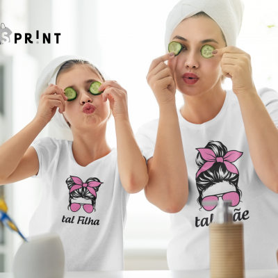 Mãe e filha vestindo t-shirts brancas com estampas semelhantes e texto 'tal mãe' e 'tal filha' em ambiente doméstico de banheiro.
