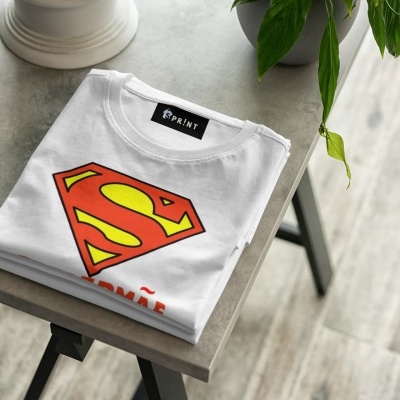 Camiseta branca com símbolo do Super-Homem dobrada numa mesa moderna.