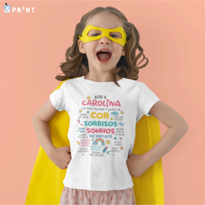 Criança com t-shirt branca com texto colorido, máscara e capa amarelas, fundo rosa.