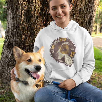 Pessoa com hoodie branco com estampa de cão junto a um cão Corgi em parque