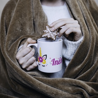 Caneca branca com nome Inês e flores segurada por mãos, mergulhando biscoito estrela decorado, com cobertor castanho