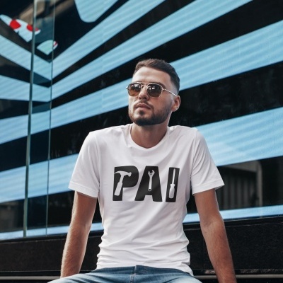 Homem com camisola branca 'PAI', jeans azuis e óculos de sol sentado