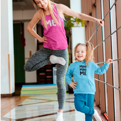 Mulher com top rosa 'ME' e leggings cinzentas e menina com casaco azul 'MINI MINI ME' e calças azuis numa sala com chão de azulejo