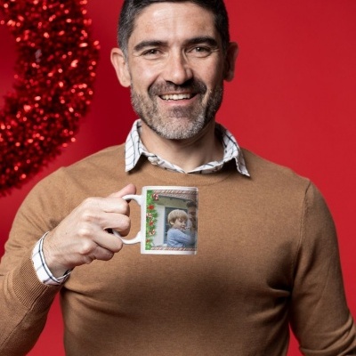 Homem a sorrir segurando uma caneca com foto e decoração natalícia, fundo vermelho