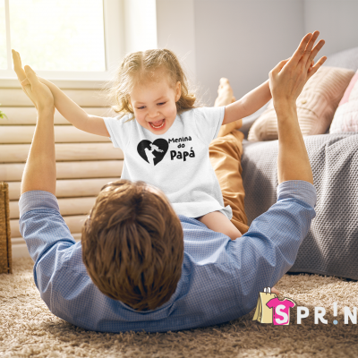 Camisola branca infantil com texto Mamã e Papá sentada na barriga de adulto deitado em tapete numa sala