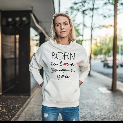 Mulher com hoodie branco com texto 'BORN to Love you' e calças de ganga azuis numa rua urbana