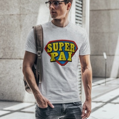 Homem vestido com camiseta cinza clara com estampa SUPER PAI, jeans rasgados cinza e mochila castanha em ambiente urbano
