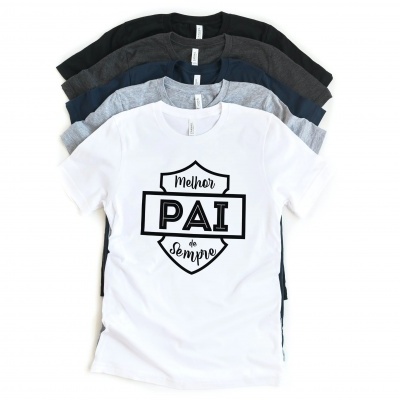 Cinco t-shirts de diferentes cores empilhadas, t-shirt branca com texto preta 'Melhor PAI de Sempre' no topo.