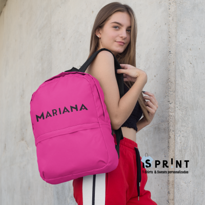 Mochila rosa personalizada com nome usada pela jovem junto à parede de cimento