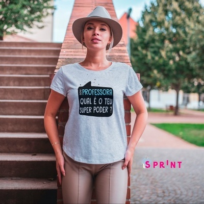 Mulher com t-shirt cinzenta clara com texto sobre ser professora em ambiente exterior